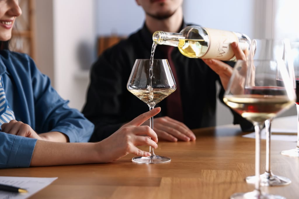 Tarjoilija kaataa valkoviiniä lasiin, jota nainne pitää kädellään.