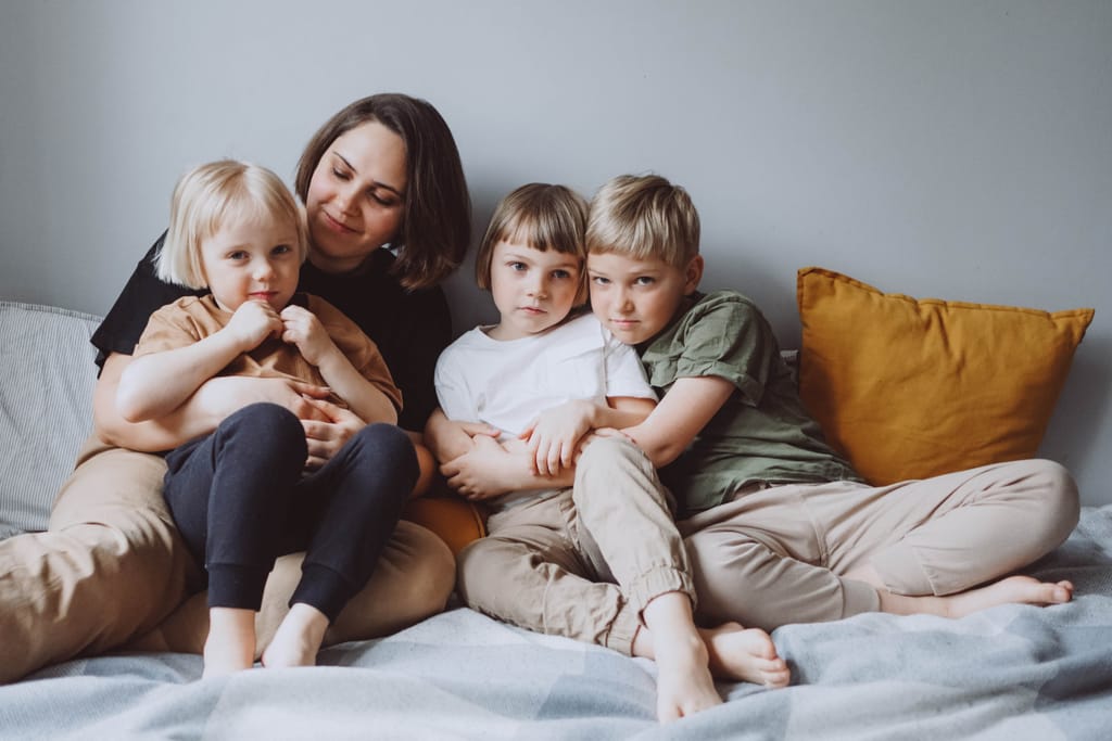Äiti sängyllä kolmen lapsen kanssa. Yksi lapsista sylissä.