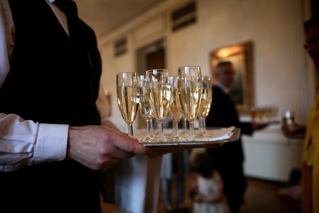 Tarjoilija kantaa kädessään tarjotinta, jossa useita kuohuviinilaseja.