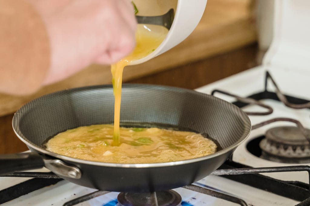 Henkilö kaataa munakasmassaa pannulle.