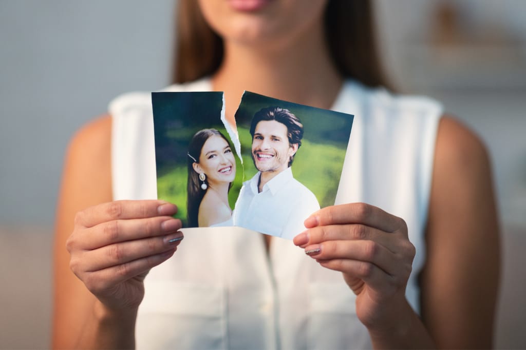 Nainen pitää käsissään kahtia revittyä valokuvaa pariskunnasta.