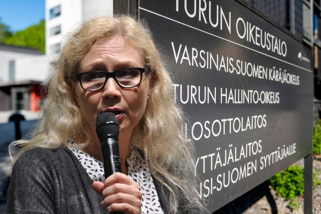 Anneli Auer puhuu mikrofoniin Turun oikeustalon edessä Varsinais-Suomen käräjäoikeuden kyltin vieressä.