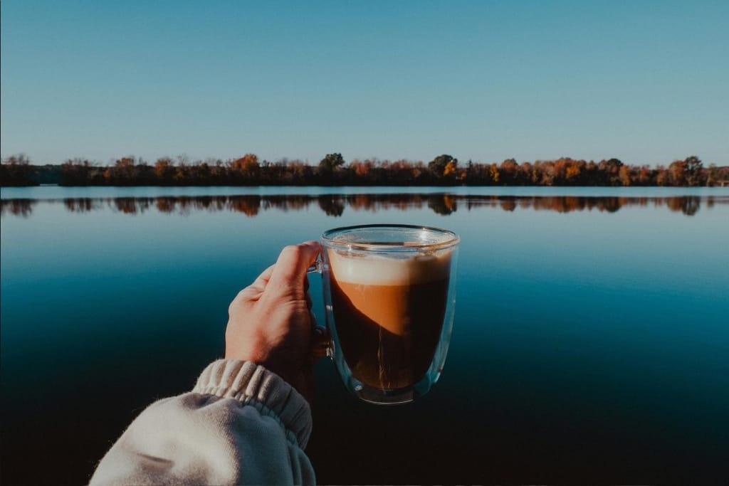 kahvikuppi kädessä järvimaisemassa aamukahvi ulkona kahvin vaikutus kehoon