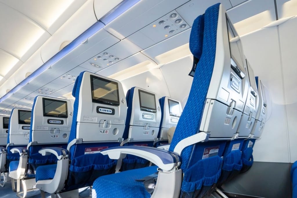 Tyhjä lentokoneen matkustamo sinisin istuimin ja selkänojanäytöin Airbus A320:ssa.