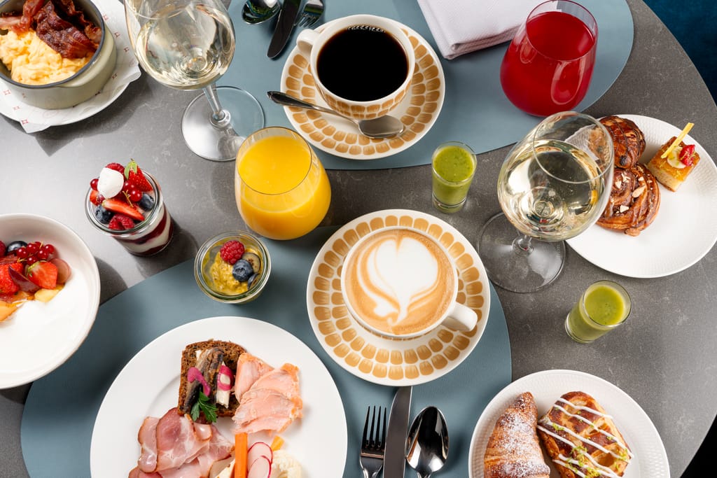 Runsas aamiaispöytä ylhäältä kuvattuna, kahvia, mehua, leivonnaisia ja erilaisia annoksia.