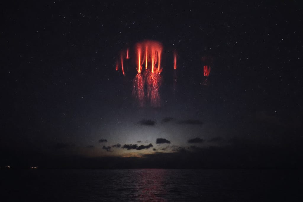 Punaiset sprites-salamat yläilmakehässä meren yllä pimeällä taivaalla