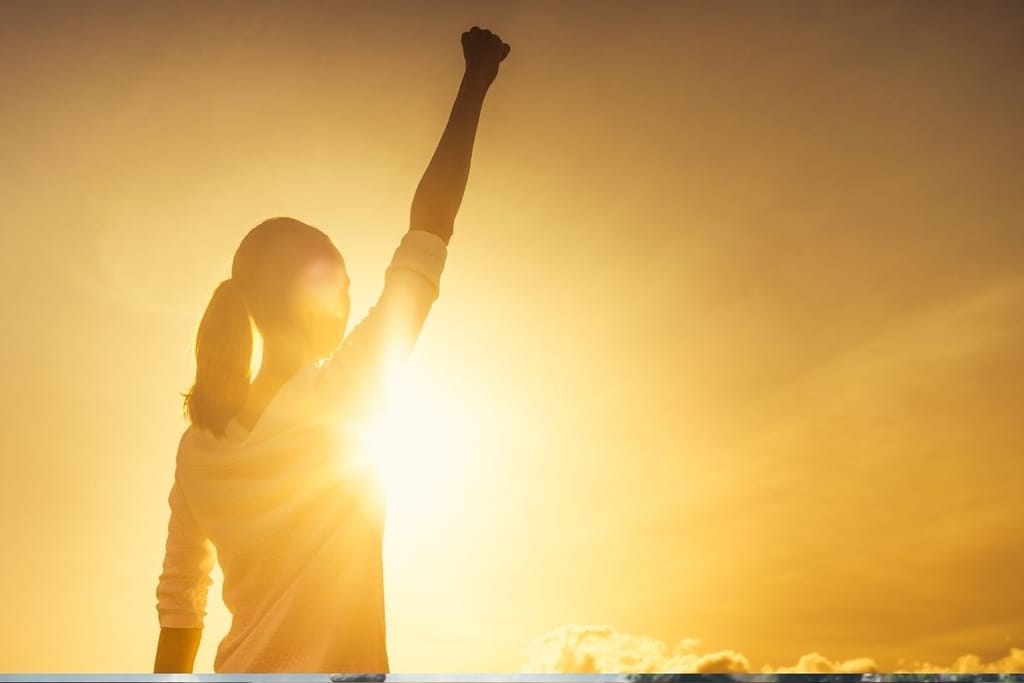 Itsevarma nainen nostaa nyrkin ilmaan auringonvalossa – itsenäisyys ja korkeat standardit