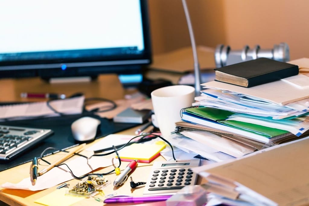 Sotkuinen työpiste tietokoneella, kahvikupilla ja papereilla – arjen epäjärjestys työpöydällä