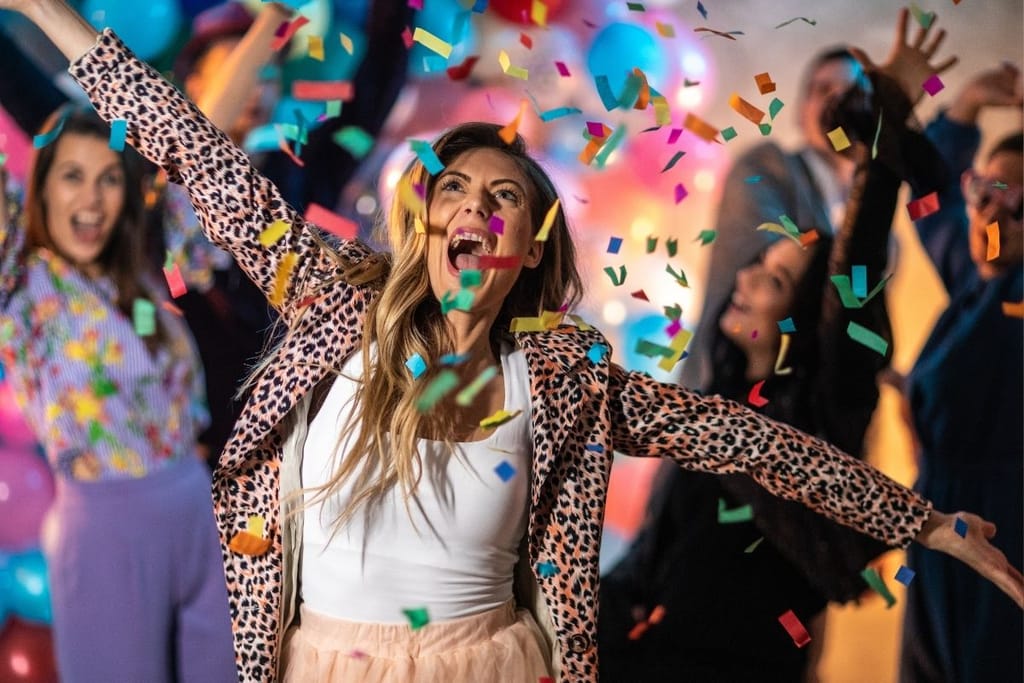 Nuori nainen leopardikuosisessa takissa juhlii käsillään ilmaan konfettisateessa vappujuhlissa.