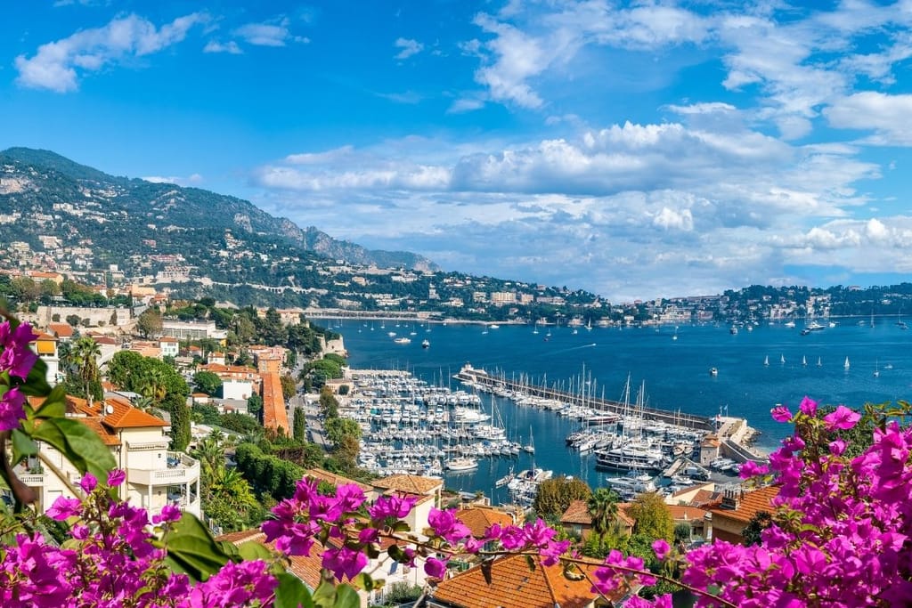 Ranskan Rivieran satamamaisema kukkivien bougainvillea-pensaiden takaa nähtynä – White Lotuksen 4. kauden kuvauspaikka.