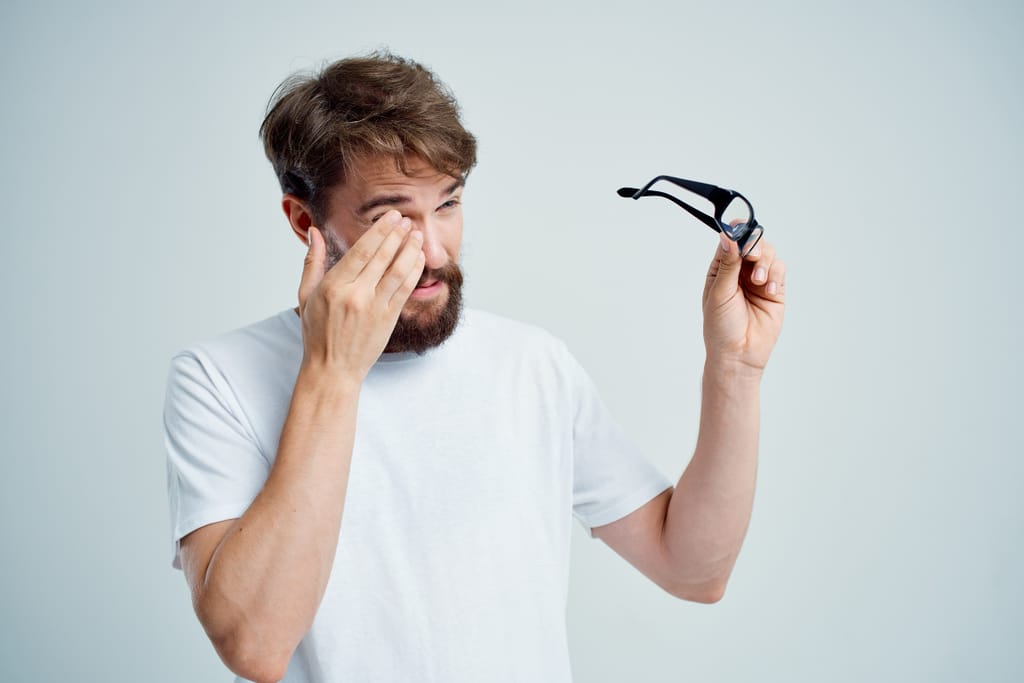 Mies hieroo silmiään ja pitelee silmälaseja toisessa kädessä.