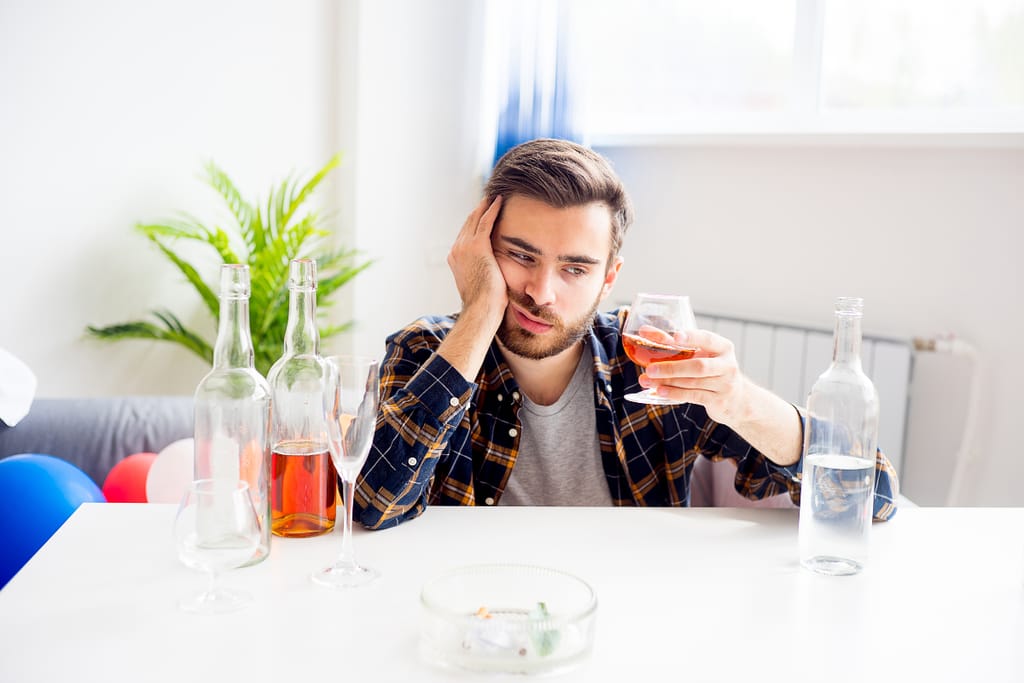 Mies istuu pöydän ääressä ja nojaa poskeen. Edessä alkoholijuomia.