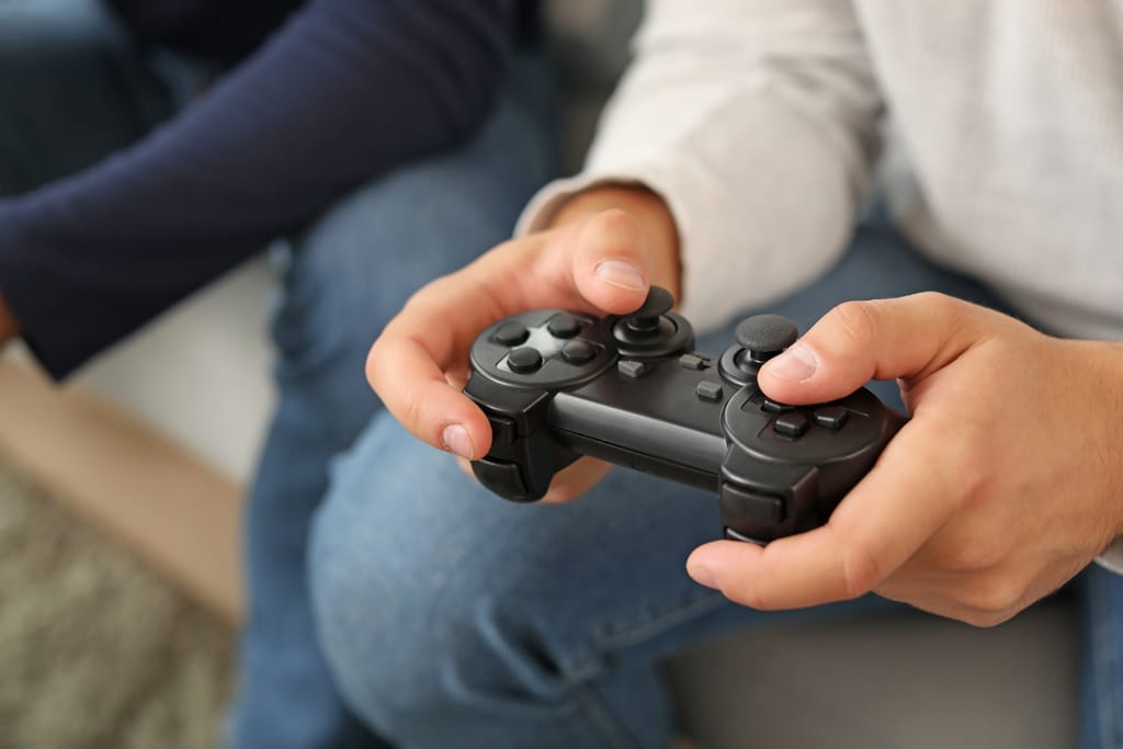 Mies istuu sohvalla ja pelaa pelikonsolilla.