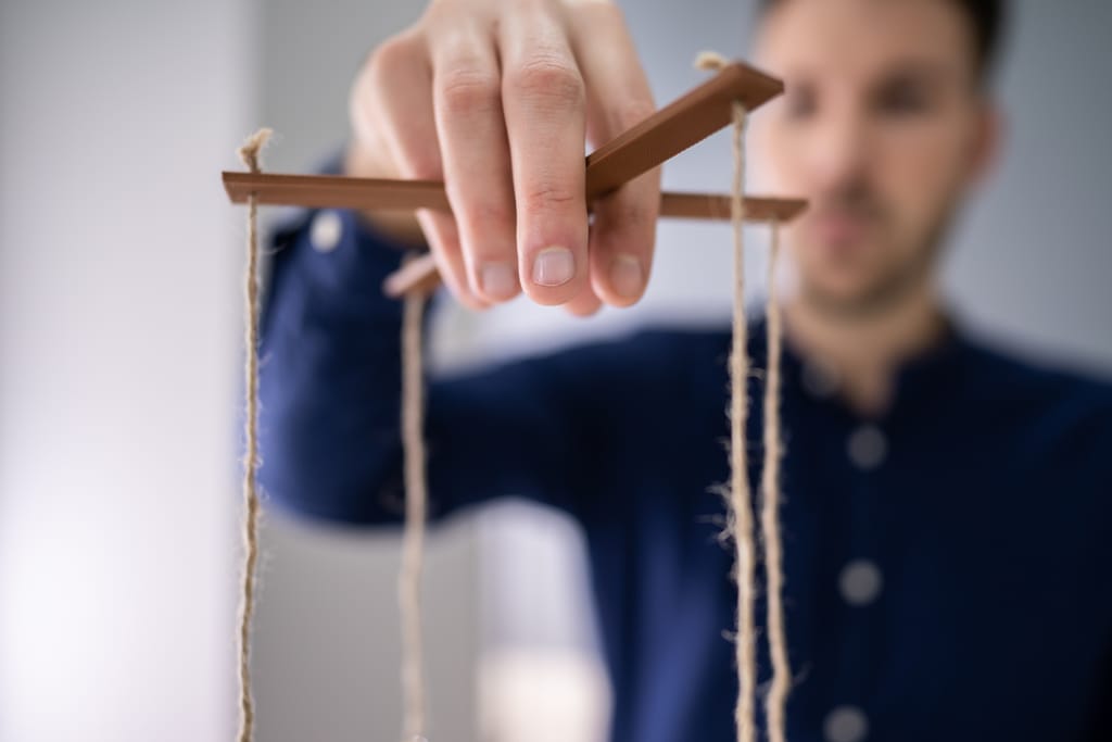 Käsi pitelee marionettinukkeohjainta lähikuvassa.