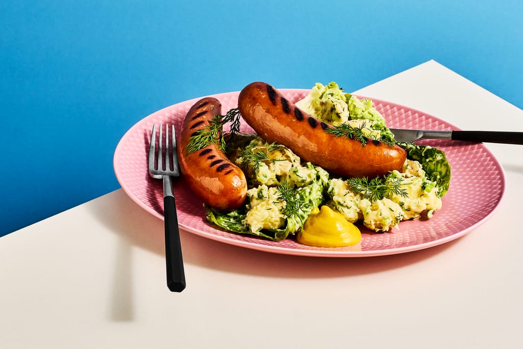 Lautasella kaksi makkaraa ja alla salaatteja.