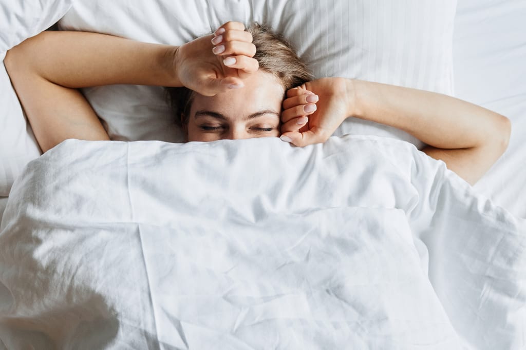 Nainen makaa sängyssä peiton alla silmät kiinni.