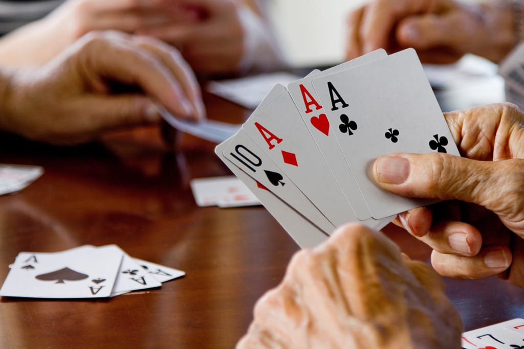Kädessä pelikortteja, taustalla menossa korttipeli.