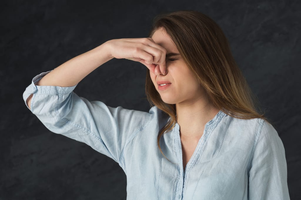 Nainen pitelee nenäänsä pahan hajun vuoksi ja irvistää.