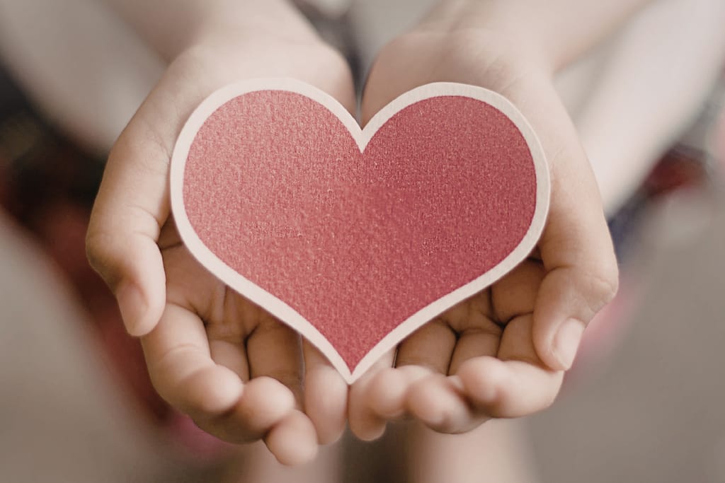 Käsi pitelee paperisydäntä.