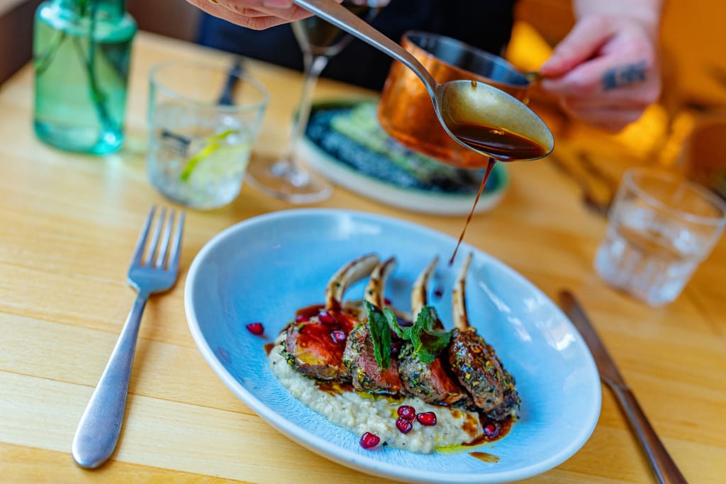 Ravintolapöydässä annos, jossa karitsankaretta ja kastiketta.