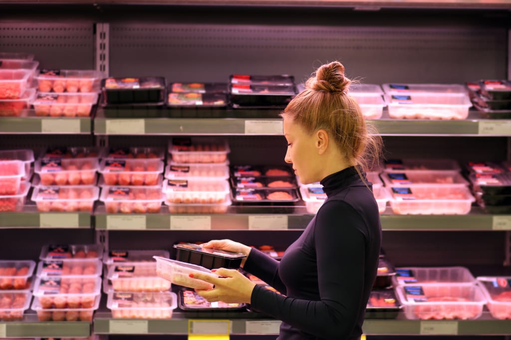 Nainen valitsee pakettia kaupan lihaosastolla.