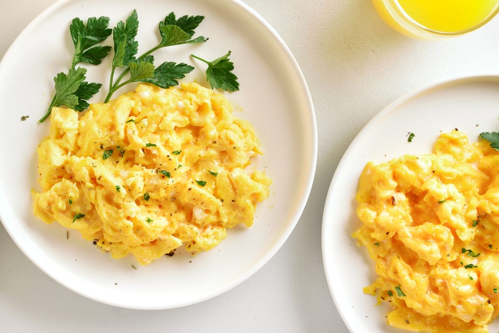 Kaksi lautasta, joilla munakokkelia. Päällä persiljaa.