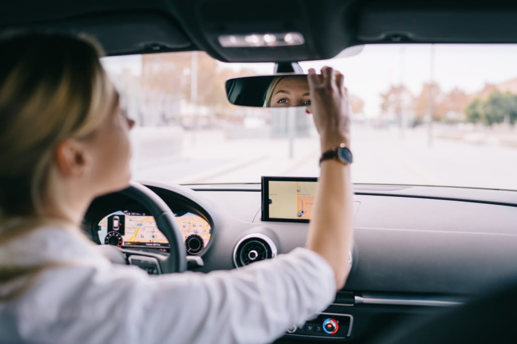 Nainen säätää auton taustapeiliä kuljettajan paikalla.