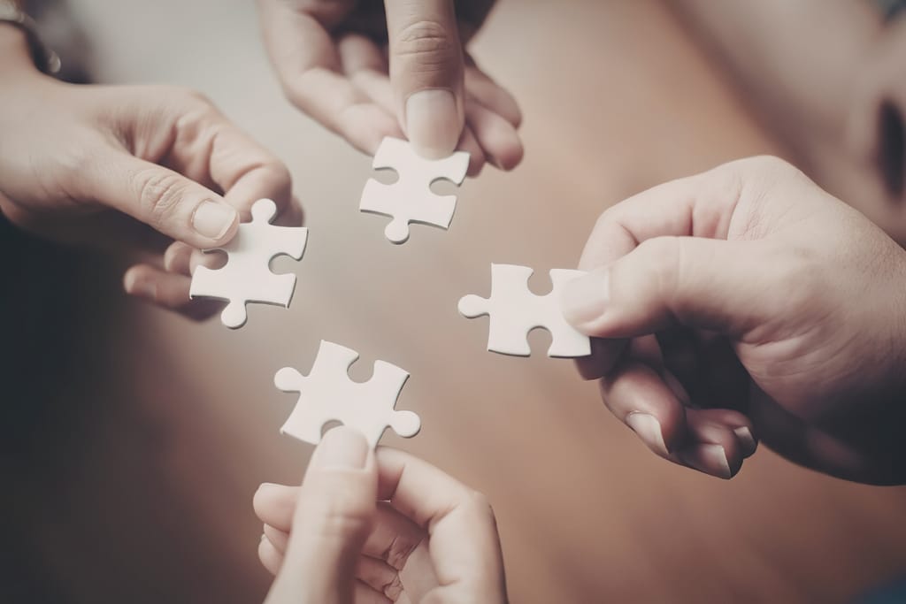 Neljä ihmistä pitää käsissään palapelin paloja toisiaan vasten.