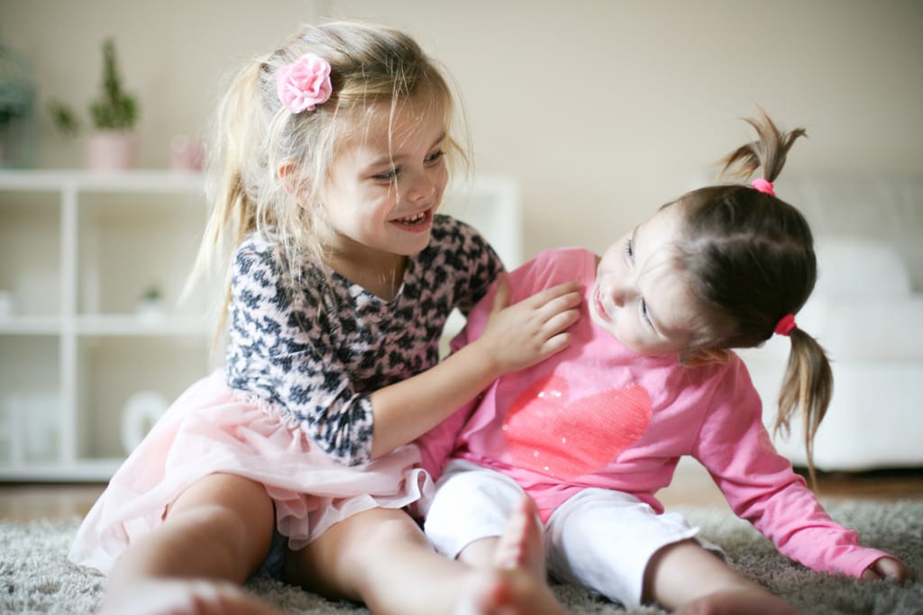 Kaksi tyttölasta leikkii kotona lattialla.