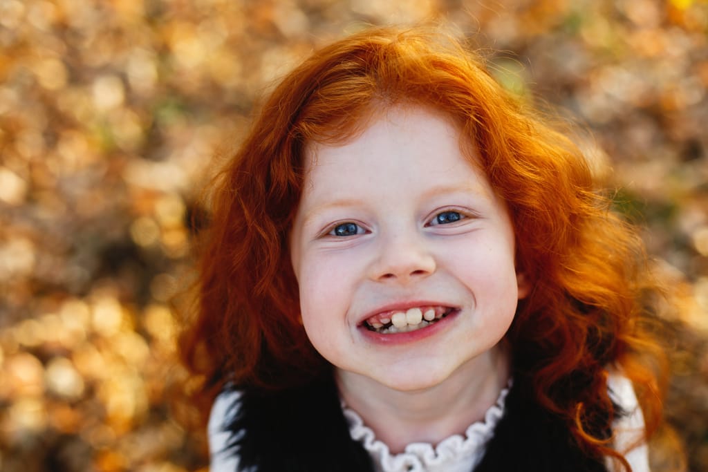 Punatukkainen poikalapsi hymyilee kameralle.