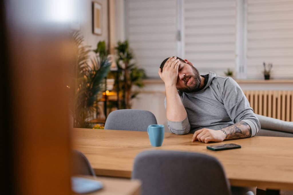 Mies istuu pöydän ääressä ja pitelee otsaansa.
