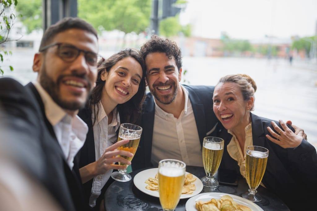 Työkavereita after workilla. Edessä sipsiä ja juomia. Iloisia ilmeitä.