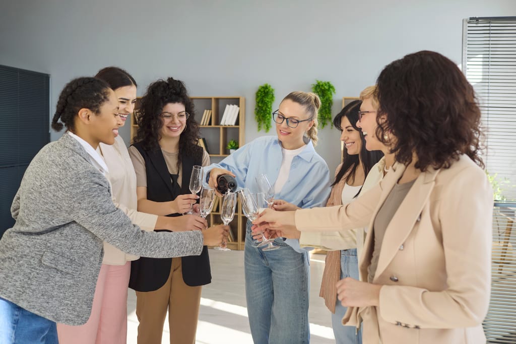 7 naista juomassa kuohuviiniä toimistolla.