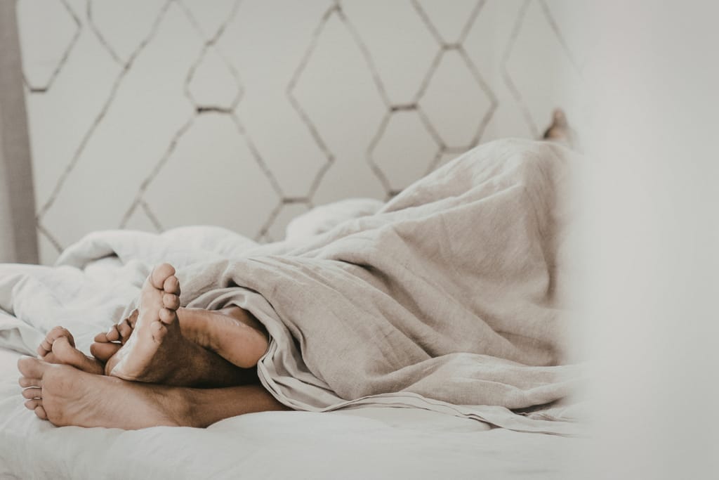Pariskunta makaa peiton alla, pelkät jalat näkyvät.
