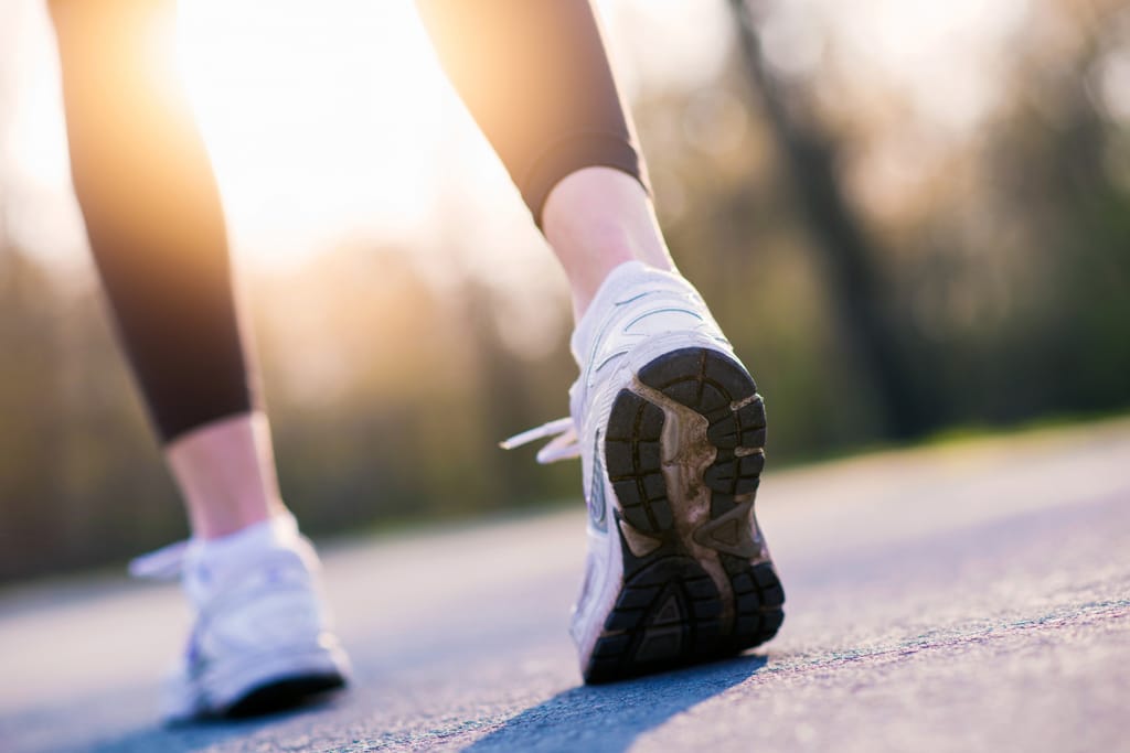 Naisen jalat. Lenkkarit jalassa, taustalla aurinko.