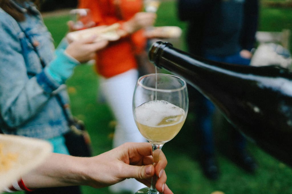 Ihmisiä ulkona, kaadetaan kuohuviiniä lasiin.