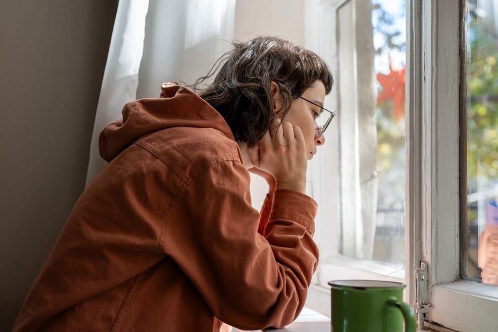 Introvertti henkilö katselee yksin ikkunasta ulos kahvikupin äärellä — yksinolo lataa introvertin akkuja