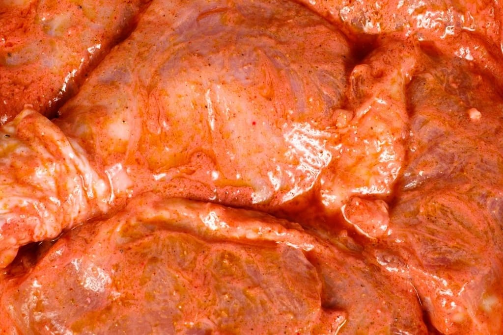 Lähikuva punaisella paprikamarinadilla marinoiduista kananpaloista raakana