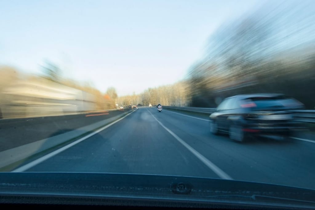 Vauhtisumeinen kuva henkilöauton tuulilasista nopeassa ohitustilanteessa moottoritiellä — auto ohittaa oikealla puolella
