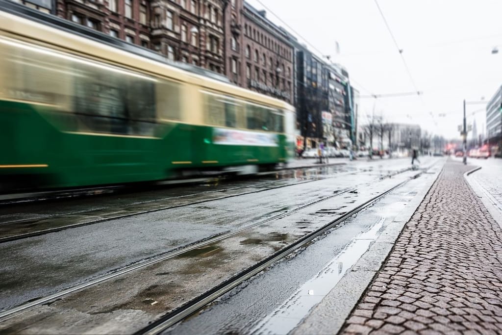 Raitiovaunu liikennöi Helsingin keskustassa ratikkakiskojen vieressä sateisella kadulla