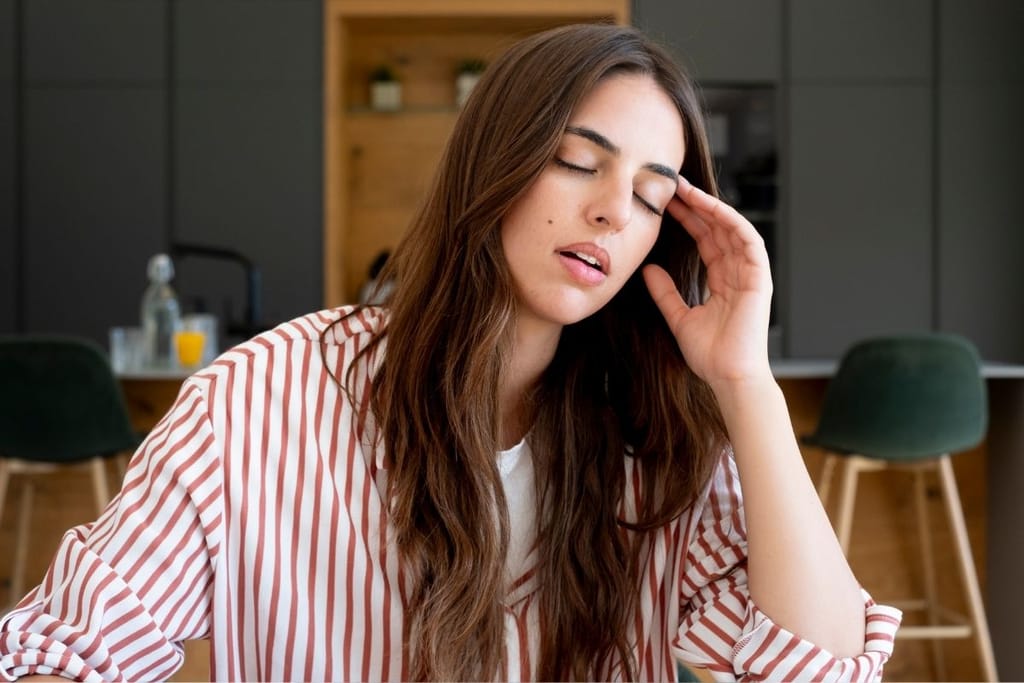 Nuori nainen pitelee kädellään ohimoaan sohvalla istuen silmät suljettuina stressin tai päänsäryn vuoksi.