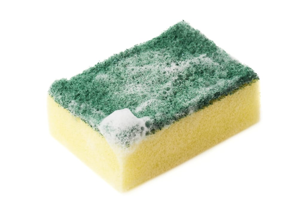 Kostea keltainen tiskisieni ja saippuavaahto tiskialtaan puhdistukseen.