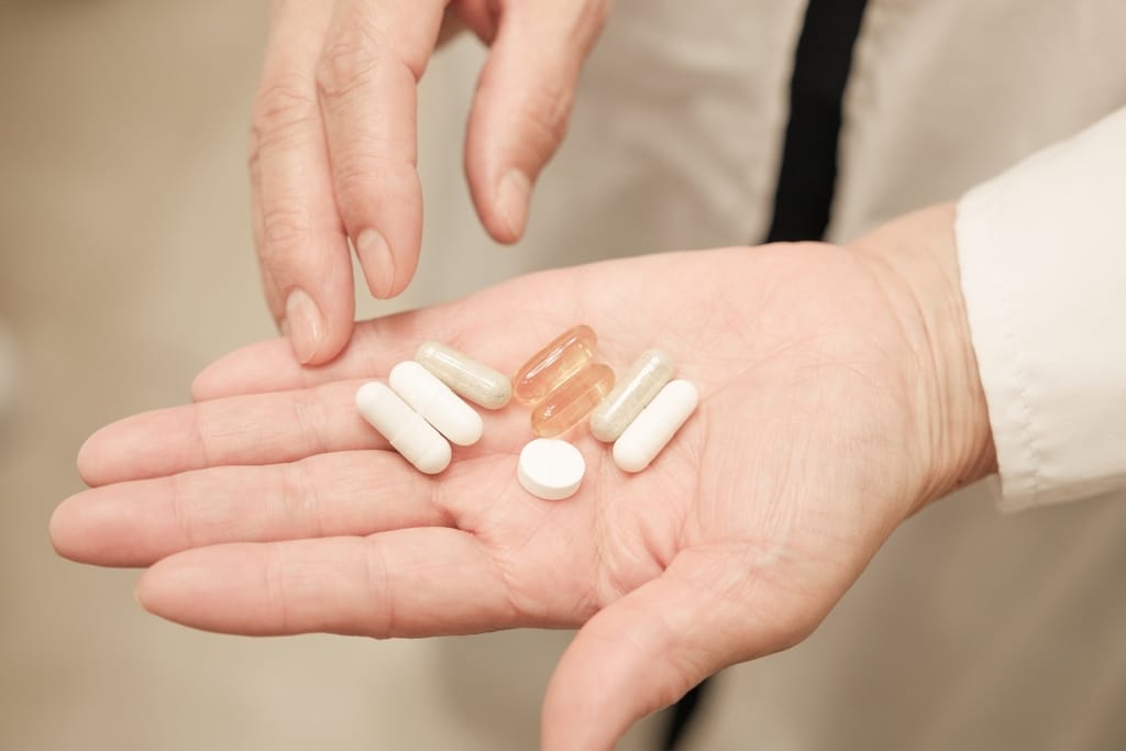 Kämmenellä on erilaisia valkoisia ja läpinäkyviä lääkekapseleita sekä pilleri.