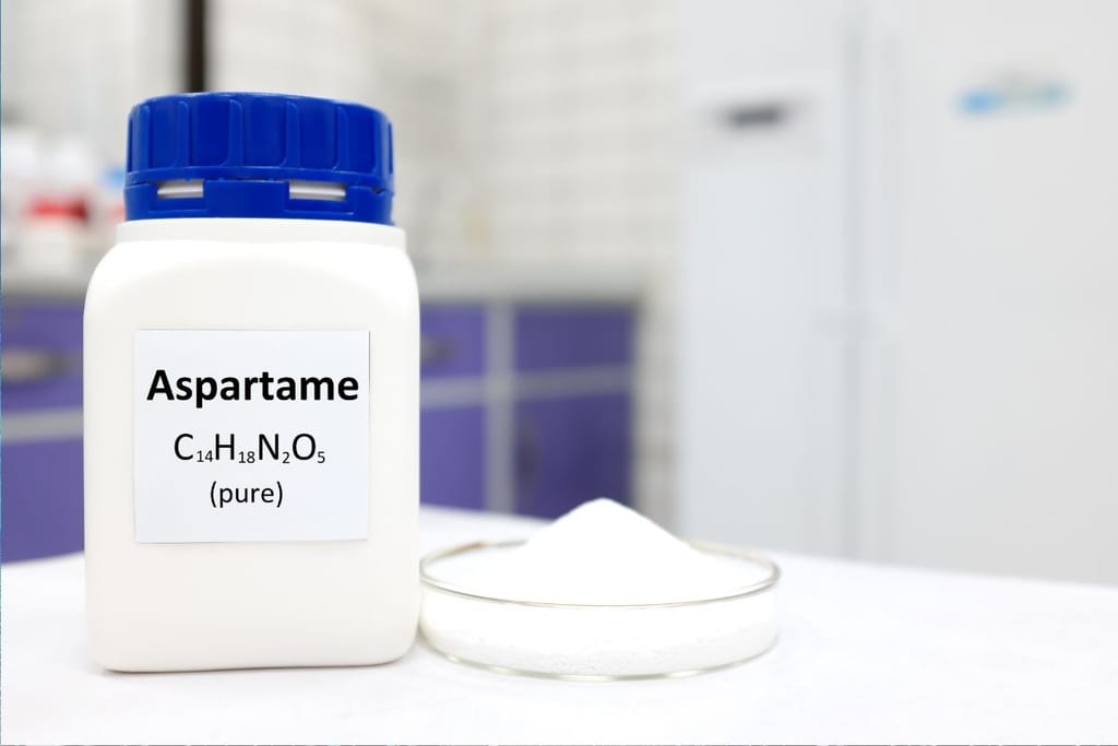 Valkoinen purkki, jossa lukee Aspartame, ja lautasella valkoista makeutusainejauhetta laboratoriossa.