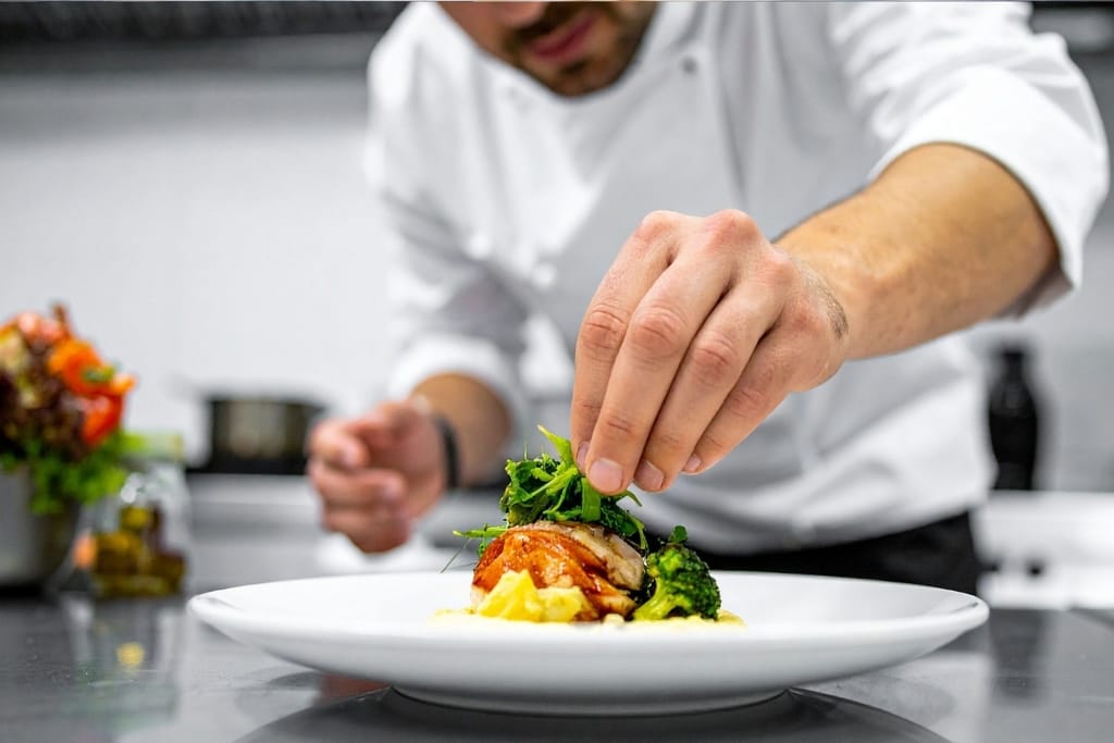 Keskittynyt kokki valkoisessa asussa ja hatussa asettelee huolellisesti fine dining -annosta ravintolassa.