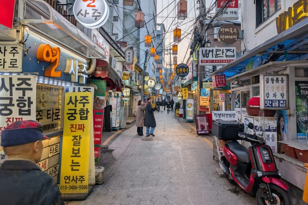 Kapea ja tunnelmallinen katu Soulin kaupungissa Etelä-Koreassa, jossa on koreankielisiä mainoskylttejä ja keltaisia lyhtyjä.