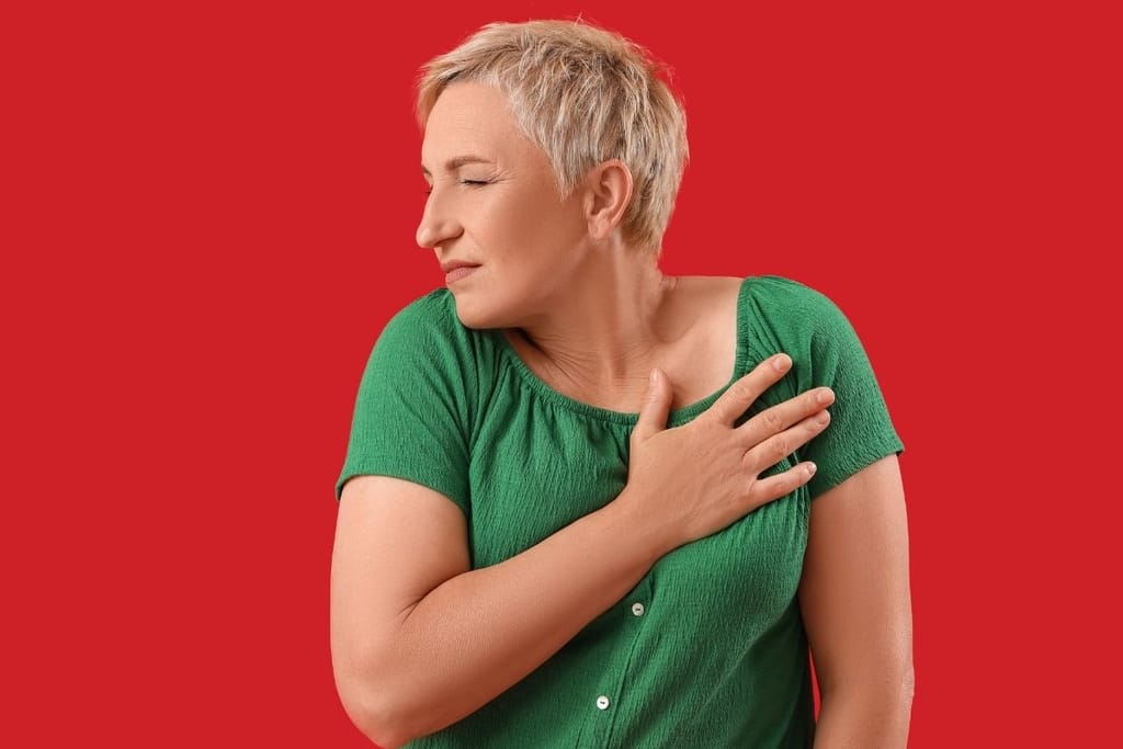 Keski-ikäinen nainen pitelee kättään rinnallaan kivuliaan näköisenä punaisella taustalla.