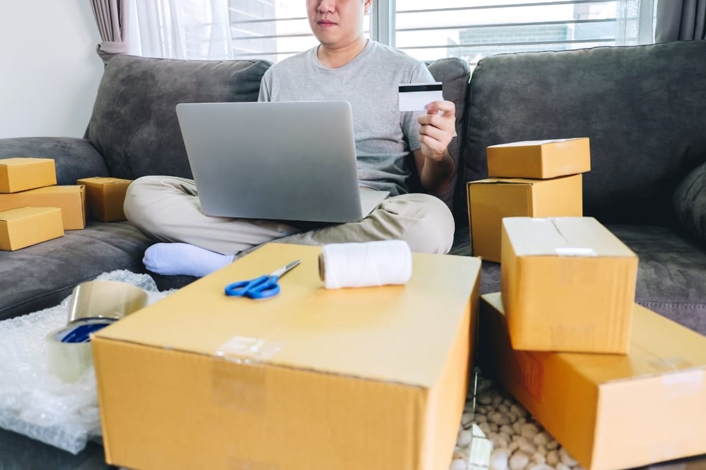 Verkko-ostoksia tekevä henkilö kannettavan tietokoneen, maksukortin ja pakettien keskellä.