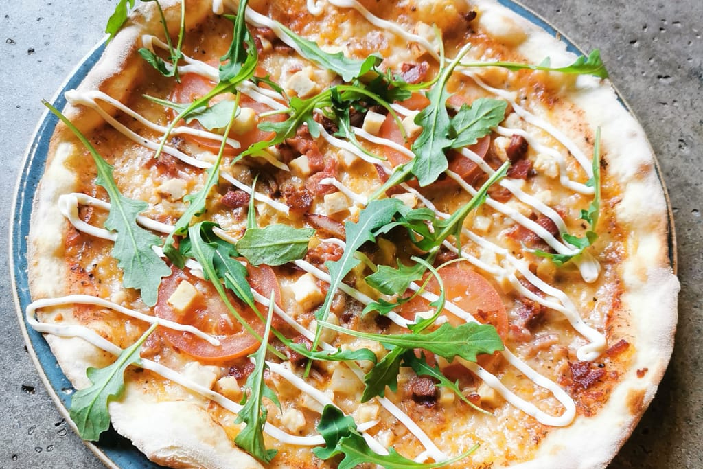 Niska Turku -ravintolan SYÖ!-annos. Pizza, jonka päällä kanaa, tomaattia ja rucolaa.