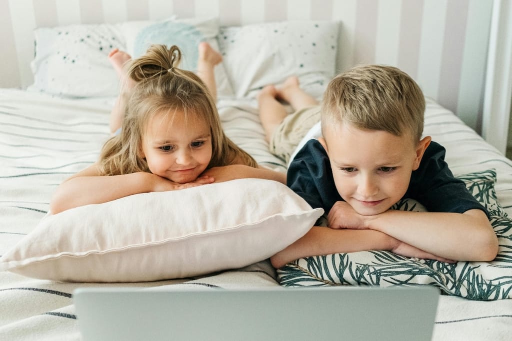 Pieni tyttö ja poika katsovat yhdessä ruutua sängyllä makoillen.